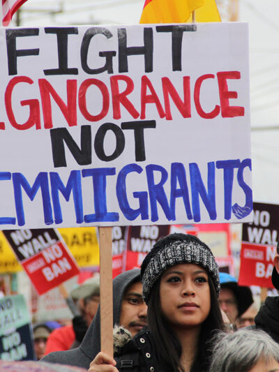 A protester holding a sign with the text "fight ignorance not immigrants"