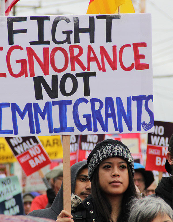 A protester holding a sign with the text "fight ignorance not immigrants"