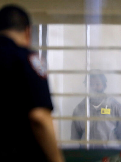 An incarcerated prison looking at a corrections officer separated by bars and a thick plastic barrier.