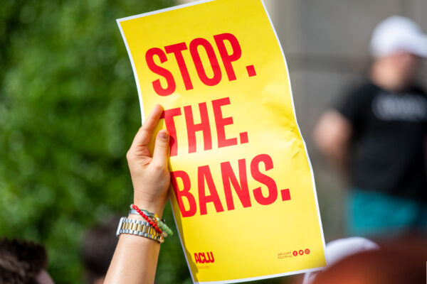 Person holding yellow poster with red words that read "Stop. The. Bans."