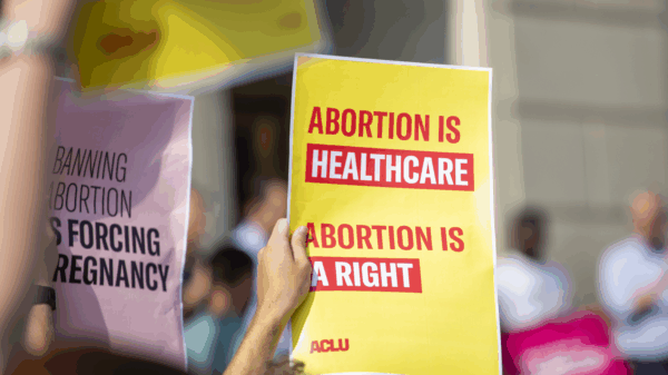 Person holding yellow poster with red lettering reading "Abortion is healthcare. Abortion is a right."
