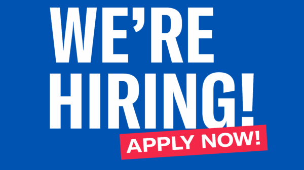 Blue background with white lettering reading "We're Hiring!" Below, "apply now!" written in white on red box placed over the bottom of "hiring" at an angle.