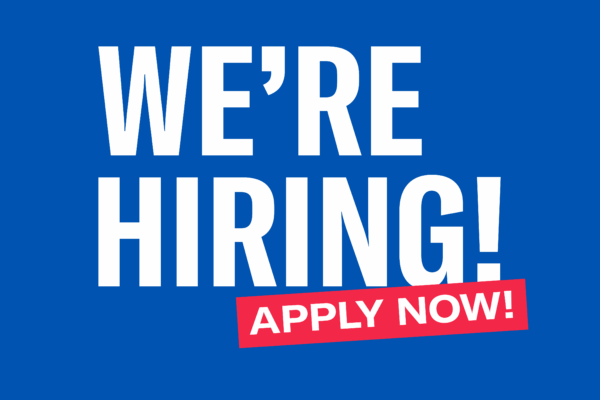 Blue background with white lettering reading "We're Hiring!" Below, "apply now!" written in white on red box placed over the bottom of "hiring" at an angle.