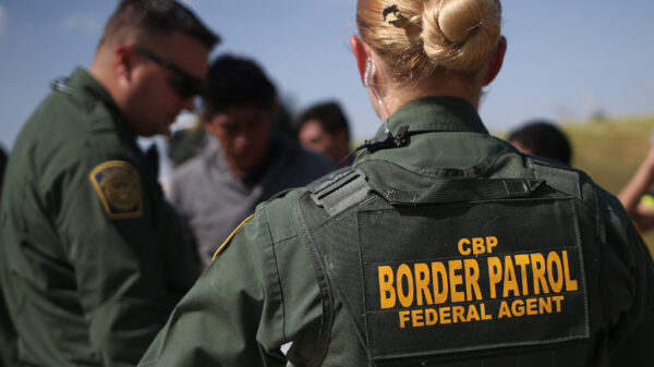 View of CBP agent from the back with green uniform and marking reading "CBP / Border Patrol / Federal Agent"
