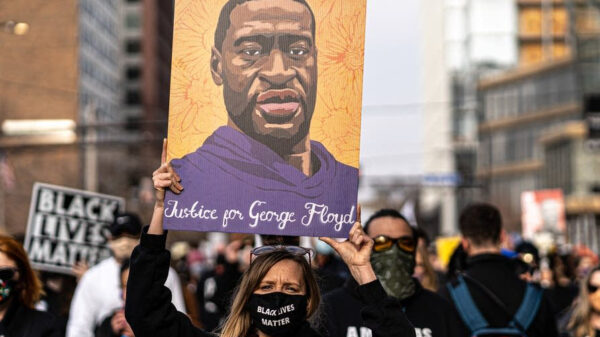 Racial justice protester wearing a Black Lives Matter mask and holding a poster above their head depicting a portrait of George Floyd