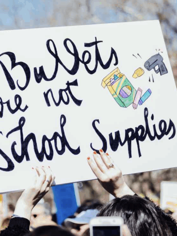 Student holding protest poster reading "bullets are not school supplies"
