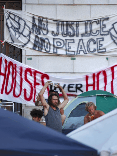 Banners hanging on Portland City Hall reading "No justice no peace" and "houses over hotels"