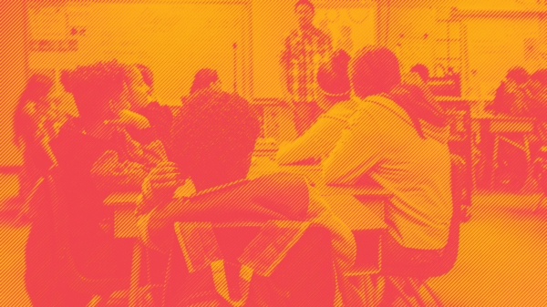 Students sitting at desks in classroom with teacher in front of class. Photo is in an orange and red duotone effect.