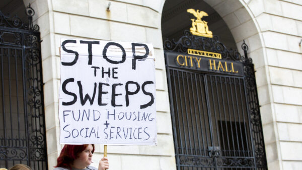 Person holding poster reading "stop the sweeps / fund housing + social services" in front of Portland City Hall.