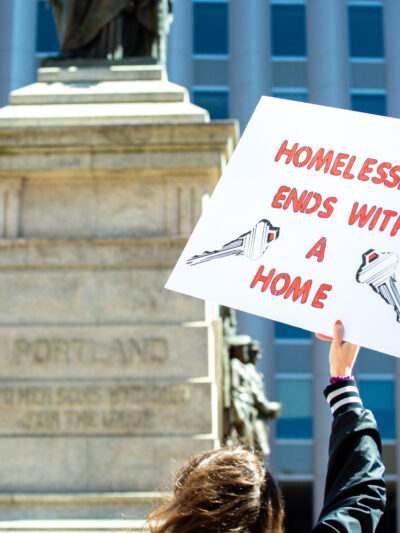 Person holding sign reading "homelessness ends with a home"