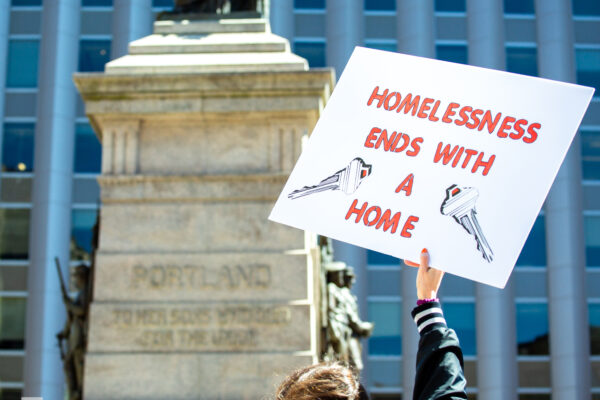 Person holding sign reading "homelessness ends with a home"