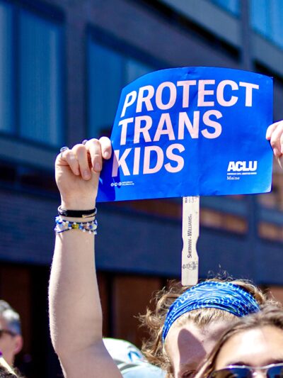 Person holding blue poster reading "protect trans kids" while marching in Portland Pride Parade, 2024.