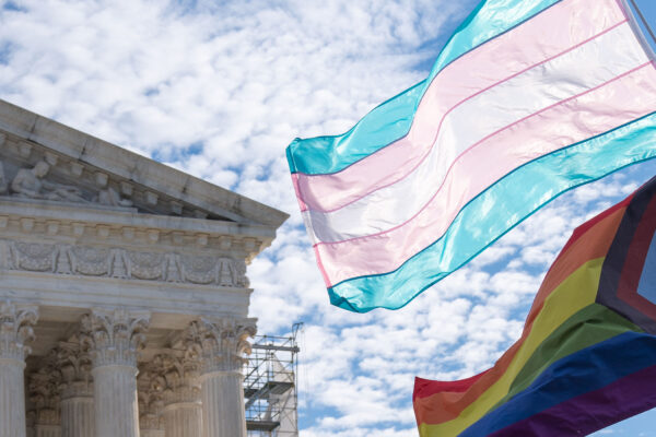 The Trans and LGBTQ+ flags waving in the wind in front of the Supreme Court Building in DC.