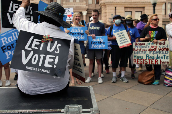 And group of demonstrators, one with a sign taped to their back saying "Let Us Vote!"