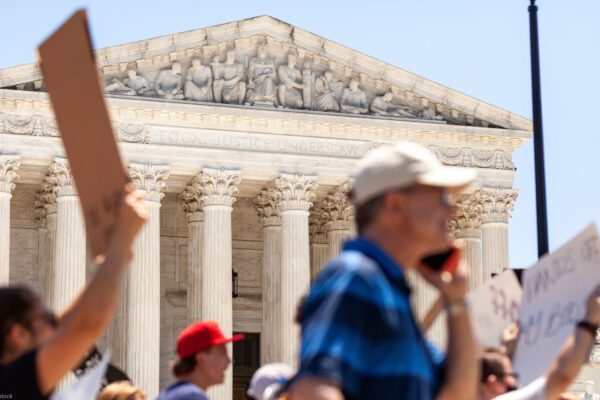 Pro-choice demonstrators (whose faces and signs are blurred) march in front of the Supreme Court and the statement on its facade, "Equal justice under law".