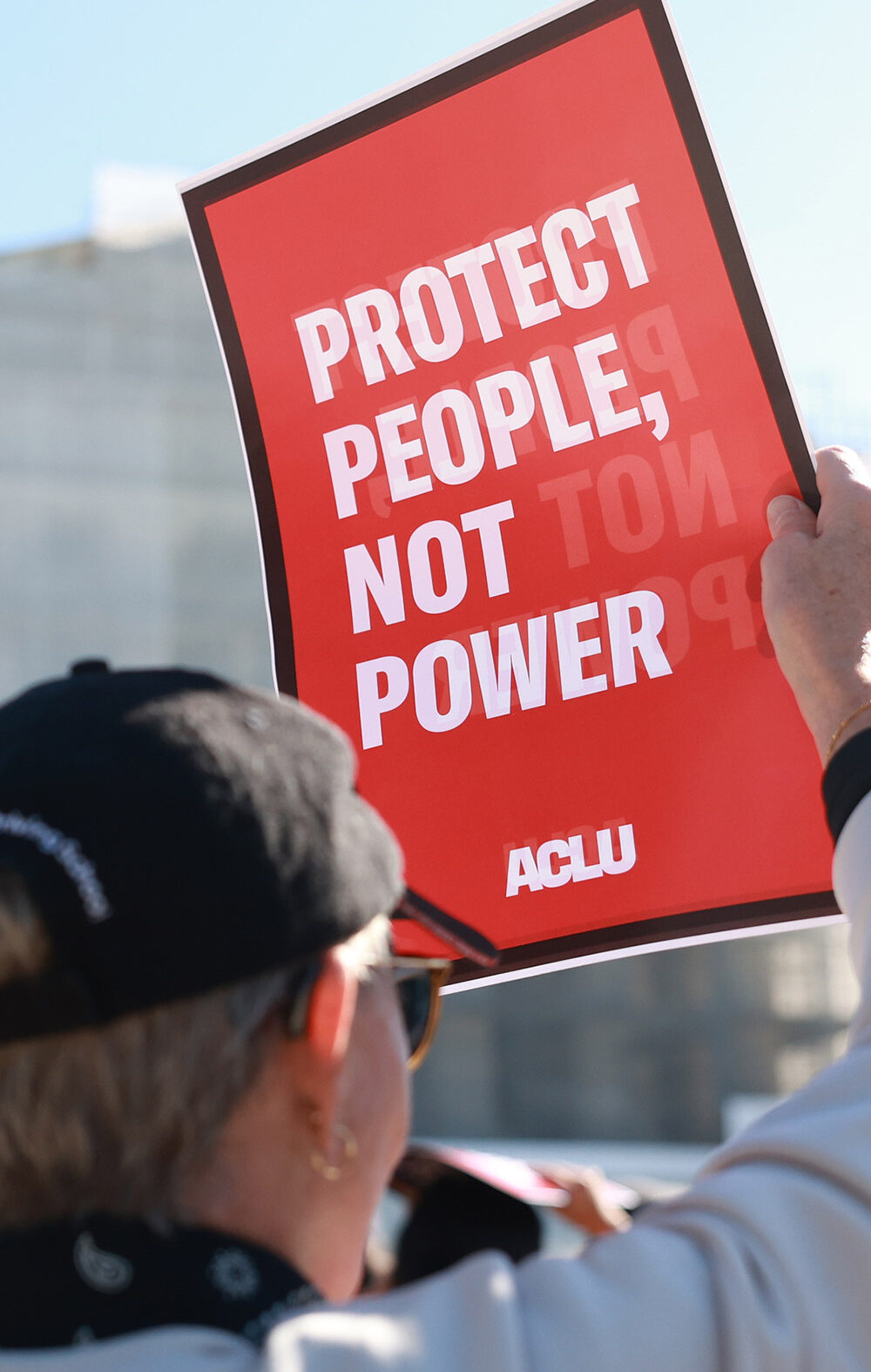 An individual holding a sign that says "Protect People, Not Power" outside of the U.S. Supreme Court ahead of arguments in the Voting Rights case Callais v. Landry.