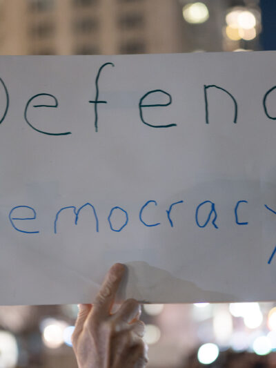 A demonstrator holding a sign that says Defend Democracy.