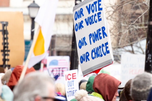 Person holding homemade protest sign reading "our vote, our voice, our power, our choice."