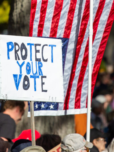 Person holding protest sign reading "protect your vote."