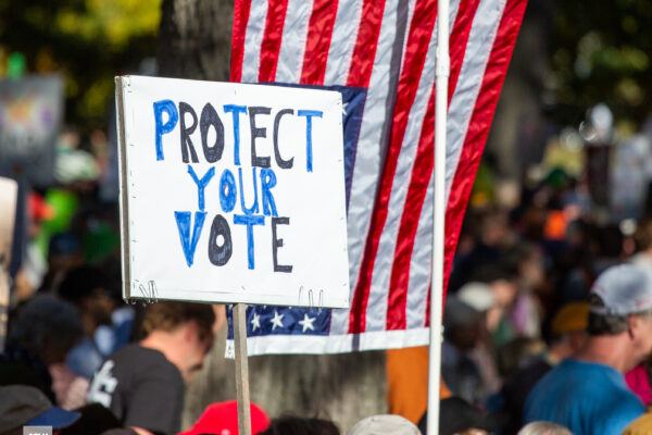 Person holding protest sign reading "protect your vote."
