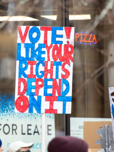 Person holding homemade protest sign reading "vote light your rights depend on it!"