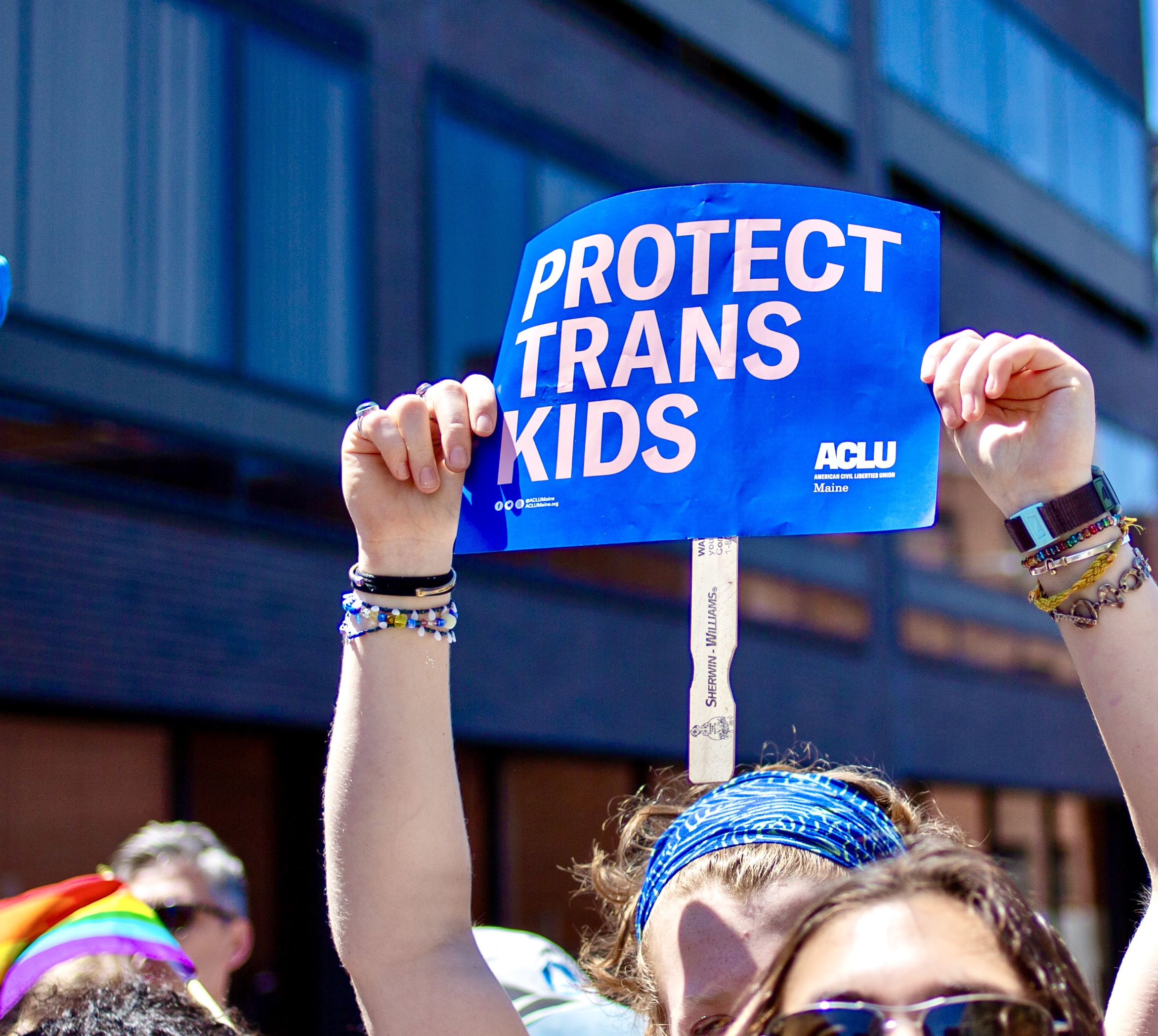 Person holding blue poster reading "protect trans kids" while marching in Portland Pride Parade, 2024.
