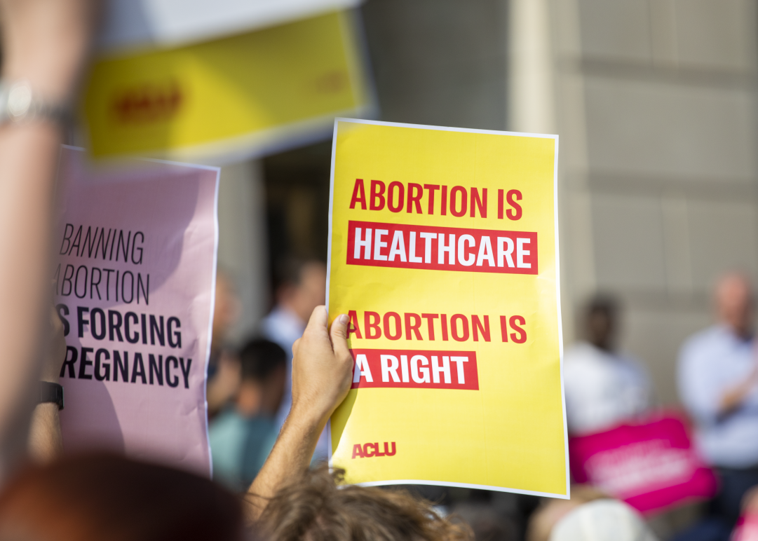 Person holding yellow poster with red lettering reading "Abortion is healthcare. Abortion is a right."