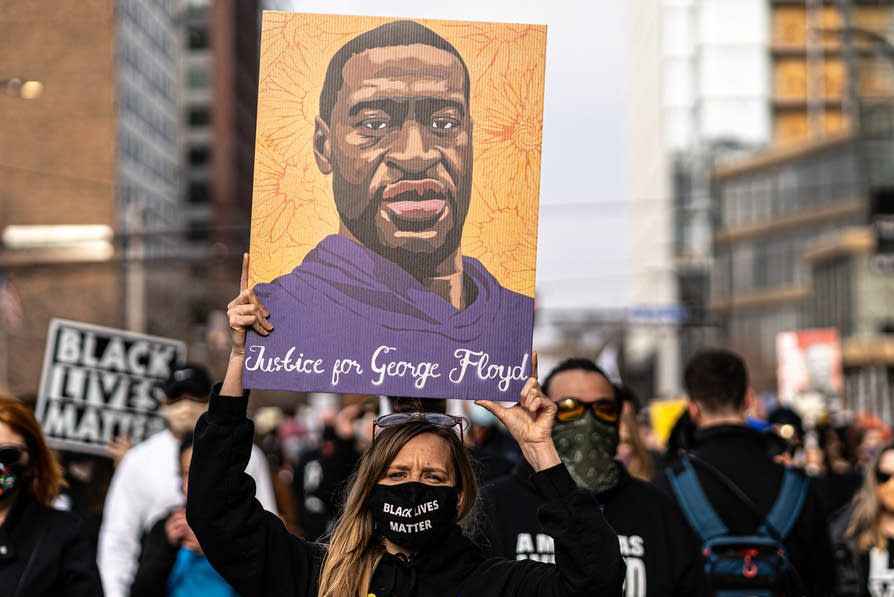 Racial justice protester wearing a Black Lives Matter mask and holding a poster above their head depicting a portrait of George Floyd