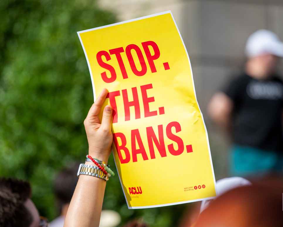 Person holding yellow poster with red words that read "Stop. The. Bans."