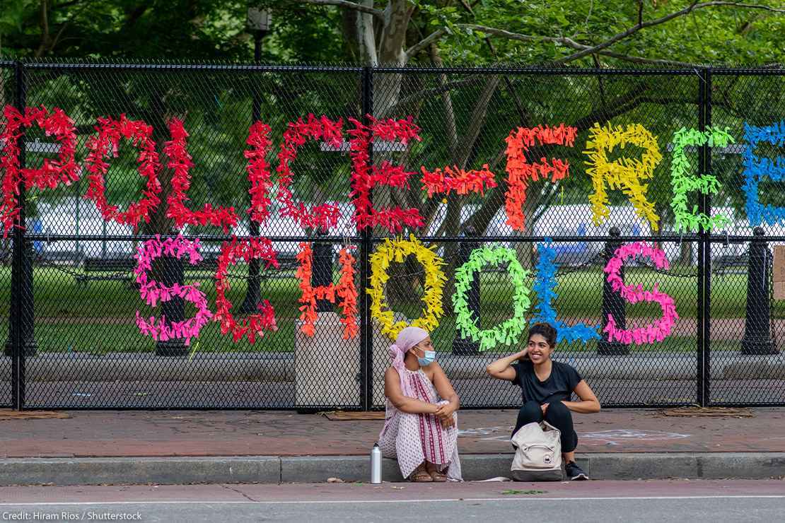 Chain link fence reading "Police-Free Schools"