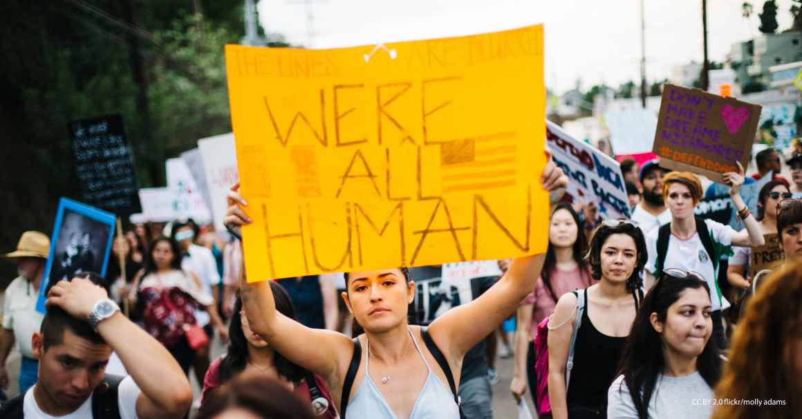 Immigrants' rights rally with woman holding sign that reads "We're All Human"