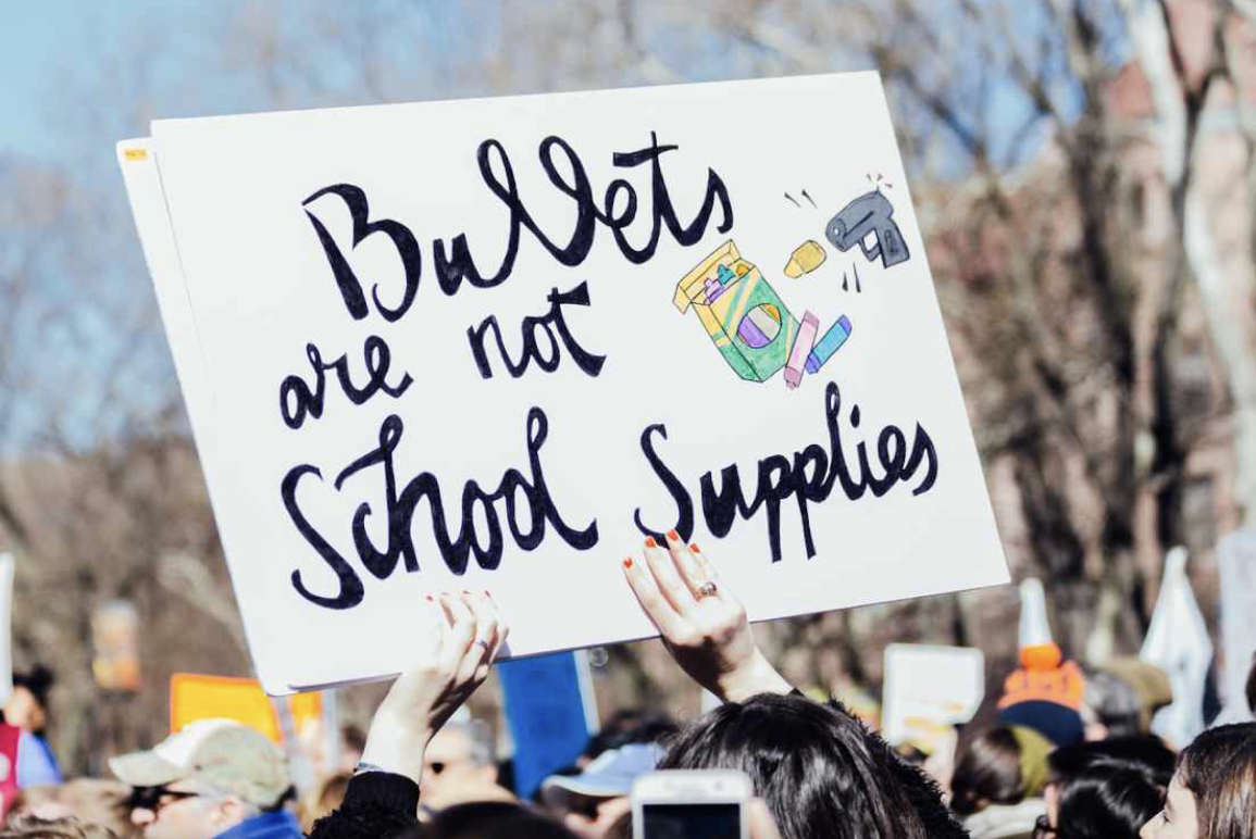 Student holding protest poster reading "bullets are not school supplies"