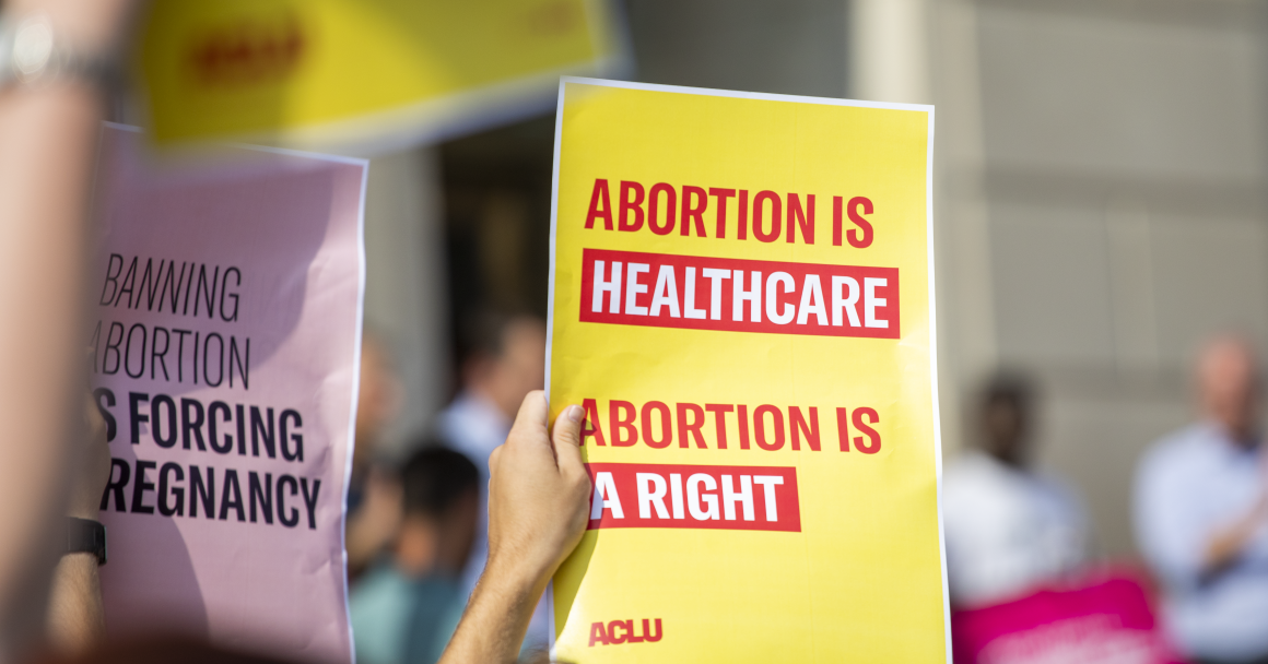 Person holding yellow poster with red lettering reading "Abortion is healthcare. Abortion is a right."