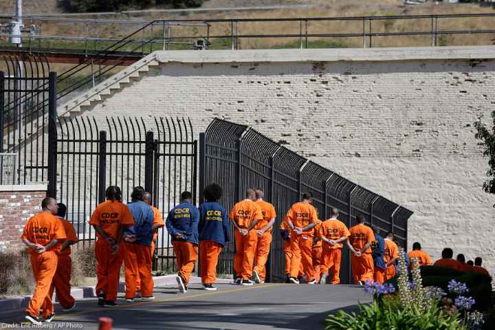 A row of general population inmates, handcuffed and in orange jumpsuits, walk in a line at San Quentin State Prison.