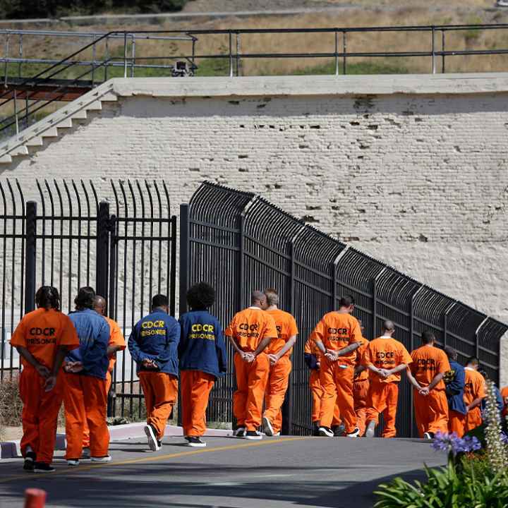 A row of general population inmates, handcuffed and in orange jumpsuits, walk in a line at San Quentin State Prison.