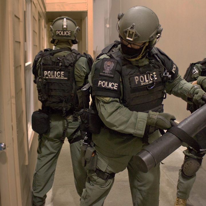 Three police officers in green uniforms preparing to knock down a door.