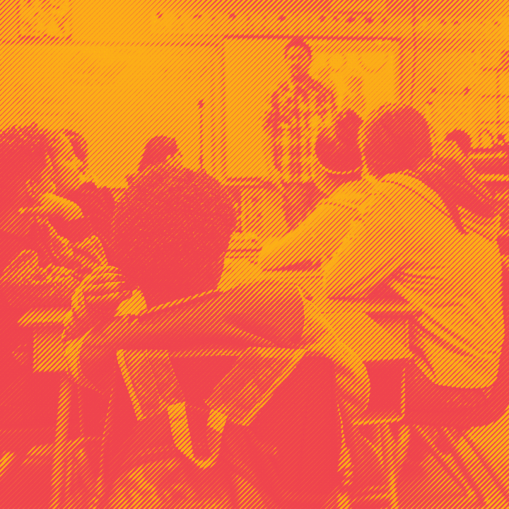 Students sitting at desks in classroom with teacher in front of class. Photo is in an orange and red duotone effect.