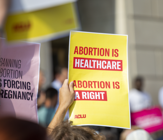 Person holding yellow poster with red lettering reading "Abortion is healthcare. Abortion is a right."